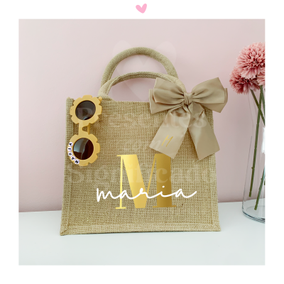 Saco de mão de ráfia com óculos de sol e laço decorativo, em fundo rosa