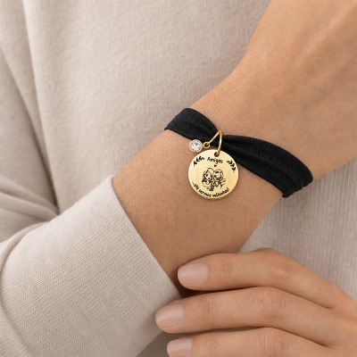 Pulseira preta com pendente dourado gravado com mensagem e ilustração