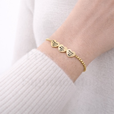 Pulseira dourada com pendentes em forma de coração com gravações em preto no pulso de uma pessoa