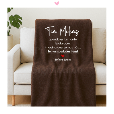 Manta castanha personalizada com texto em branco e coração vermelho sobre sofá branca.