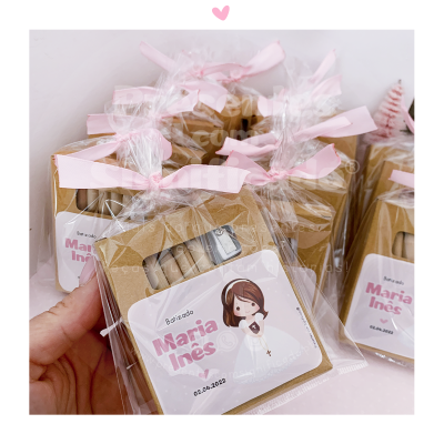 Caixas de cartão castanho com etiquetas 'Batizado Maria Inês 02.04.2022' embaladas em sacos transparentes com laços cor-de-rosa.