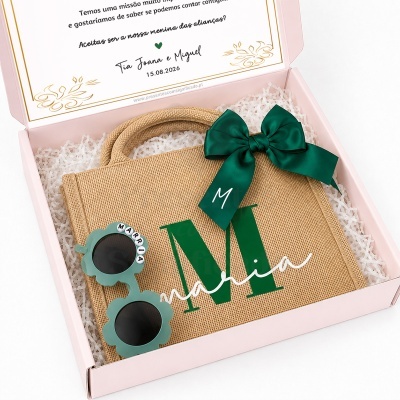 Caixa rosa com bolsa personalizada castanha, laço verde e óculos de sol com letras.