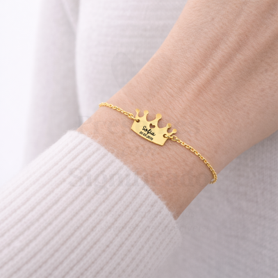 Pulseira dourada com pendente de coroa gravado Sofia 01.05.2010 no pulso de uma pessoa