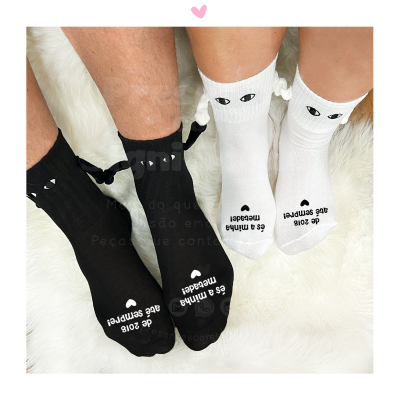 Meias pretas e brancas com detalhes de olhos, laços e texto na planta dos pés sobre tapete branco