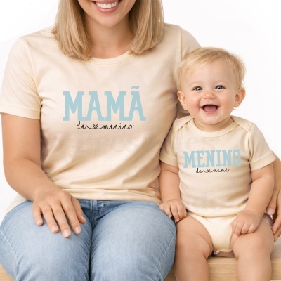 T-shirt bege clara para mãe e body bege claro para bebé com textos em azul, sentados juntos num banco de madeira
