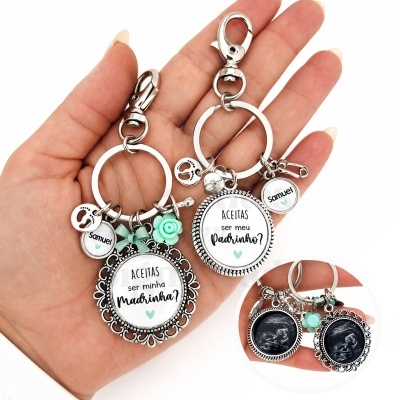 Dois porta-chaves metálicos com texto pedido para ser madrinha e padrinho, decorados com pendentes verdes e nomes.