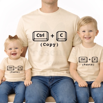 Adulto e duas crianças sentados vestindo t-shirts bege com desenhos de teclas Ctrl + C (Copy) e Ctrl + V (Paste) a preto.