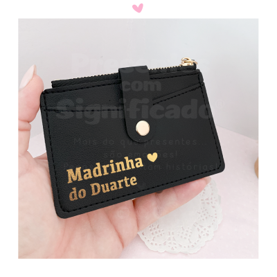 Carteira preta com texto dourado 'Madrinha do Duarte' e botão dourado, segurada por mão