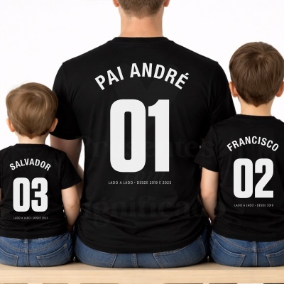 Três t-shirts pretas com nomes e números brancos para pai e filhos sentados de costas.