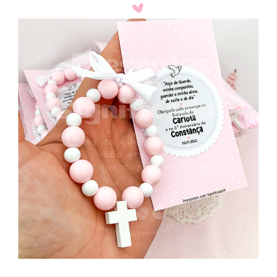 Pulseira cor-de-rosa e branca com cruz branca em cartão cor-de-rosa com texto em português