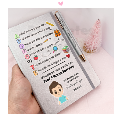 Caderno cinza com texto colorido dedicado a professora, caneta prateada e escova rosa no fundo