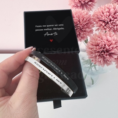 Pulseiras pretas e prateadas com texto, caixa preta com mensagem e flores cor de rosa
