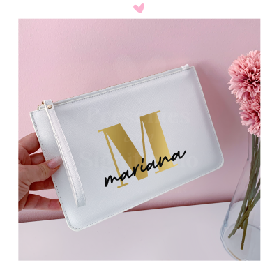 Mala branca com motivo dourado e texto preto, junto a flor rosa