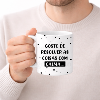 Caneca branca com texto preto GOSTO DE RESOLVER AS COISAS COM CALMA... e pontos pretos, segurada por uma mão