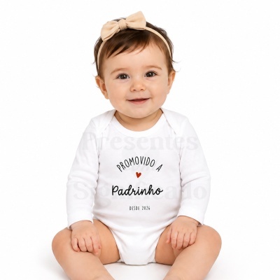 Bebé com body branco com texto PROMOVIDO A Padrinho DESDE 2026 e faixa de cabelo creme com laço
