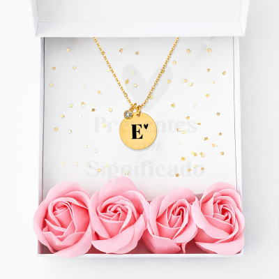 Colar dourado com pendente redondo com letra E e coração em caixa branca com confetes dourados e rosas cor-de-rosa.