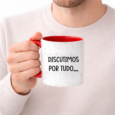Caneca branca e vermelha com texto DISCUTIMOS POR TUDO segurada por mão