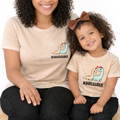 T-shirts bege com estampas de dinossauros e texto MAMASSAURUS e MINISSAURUS em mãe e filha