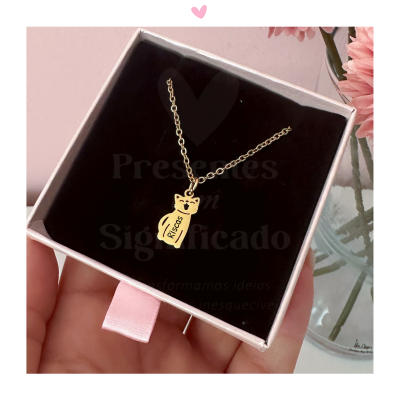 Colar dourado com pendente de gato e palavra Risca numa caixa de joias