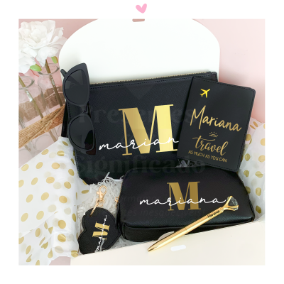 Conjunto preto e dourado com acessórios personalizados nome Mariana, incluindo bolsa, estojo, porta-passaporte, porta-chaves e caneta, acompanhado de óculos escuros e decoração de flores e papel de bolinhas