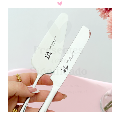 Duas espátulas metálicas para bolo com gravação seguradas por uma mão com anel dourado