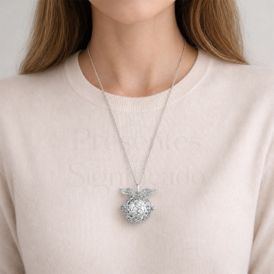 Colar de metal prateado com pendente redondo e asas, usado por pessoa com camisola bege clara.