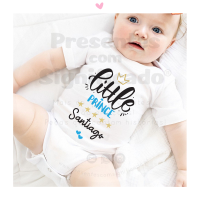 Body de bebé branco com texto colorido 'little PRINCE Santiago' e elementos decorativos, em bebé deitado
