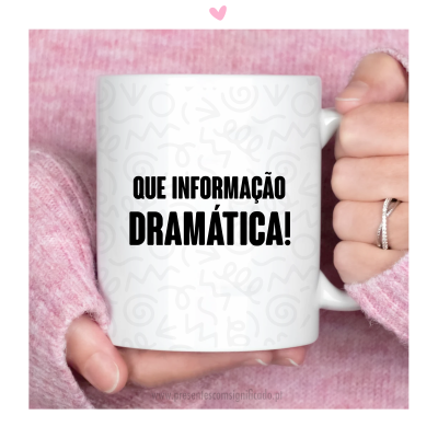 Caneca branca com texto QUE INFORMAÇÃO DRAMÁTICA! segurada por mãos com camisola rosa e anel