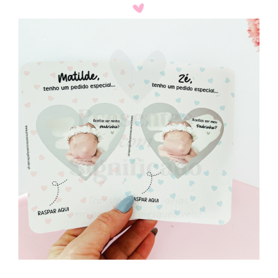 Duas cartelas brancas de pedido especial com corações rosa e azul e texto para raspar, seguradas por mão com unhas azuis, fundo rosa e branco.