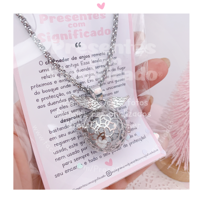 Colar prateado com pingente de esfera com asas sobre cartão com texto em português