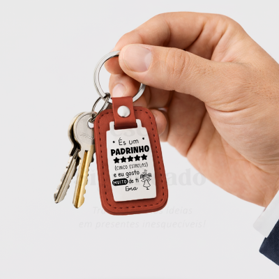 Chaveiro de pele castanha com texto em branco e preto a segurar chaves por uma mão masculina