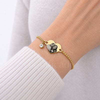 Pulseira dourada com pendente de coração gravado com foto e pedra transparente no pulso