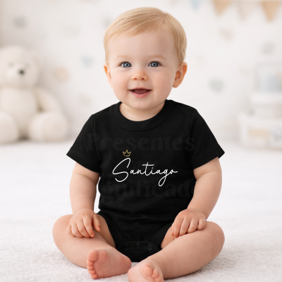 Bebé sentado com body preto com a palavra Santiago e uma coroa dourada