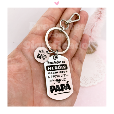 Porta-chaves metálico branco com texto em preto, no chão com fundo rosa e renda branca