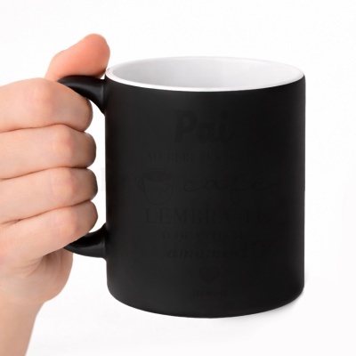 Caneca preta e branca com texto em português, segurada por mão