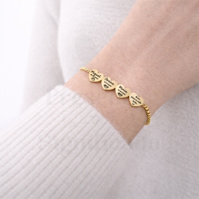 Pulseira dourada com pendentes de corações gravados no pulso de uma pessoa com camisola branca