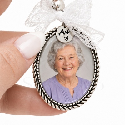Medalhão oval prateado com foto de senhora idosa, fita branca e pendente gravado com Avó.