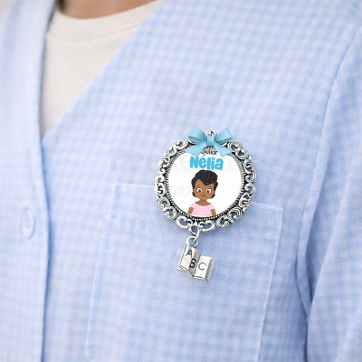 Broche prateado com laço azul e livrinho pendente, com imagem e nome Nélia em camisa azul claro xadrez