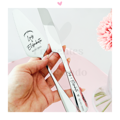 Conjunto de faca e espátula para bolo em aço inox com gravação personalizada numa mão, fundo branco e flor cor-de-rosa
