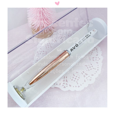 Caneta metálica rosé com tampa transparente numa caixa branca com fundo rendado branco