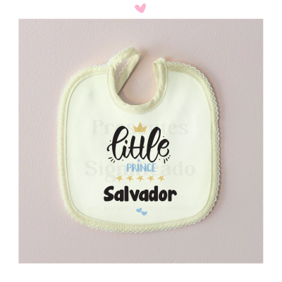 Babete branco com texto little PRINCE Salvador e detalhes dourados, fundo rosa claro.