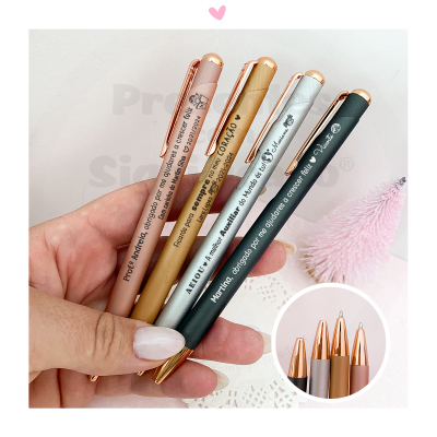 Conjunto de quatro canetas metálicas coloridas com gravações personalizadas, seguradas por mão feminina contra fundo branco.