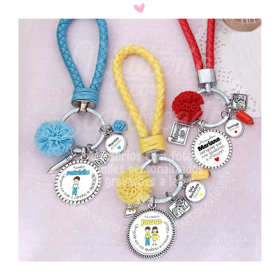 Três chaveiros coloridos com pompom e medalhas personalizadas sobre fundo rosa