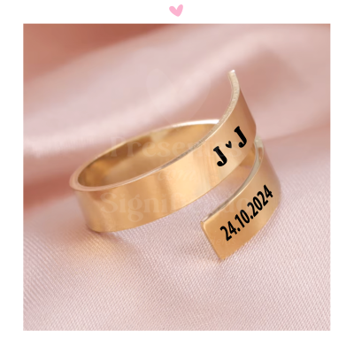 Anel dourado aberto com gravações a preto sobre tecido rosa claro