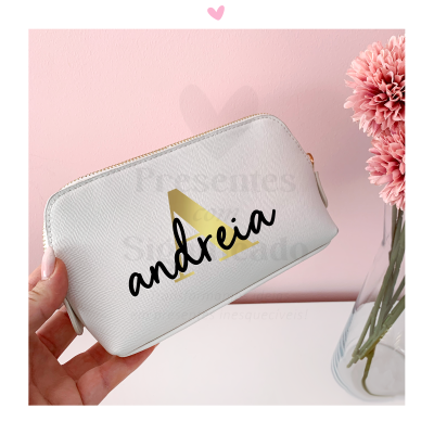 Necessaire branca com fecho dourado e nome 'andreia', mão segurando e vaso com flores cor-de-rosa