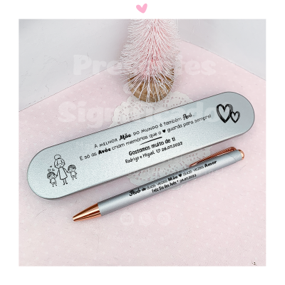 Estojo metálico prateado com caneta dourada e prateada personalizados sobre superfície rosa