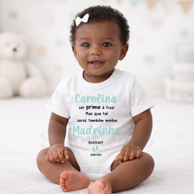 Bebé a sorrir com body branco e texto colorido sentado em ambiente claro com urso de peluche atrás