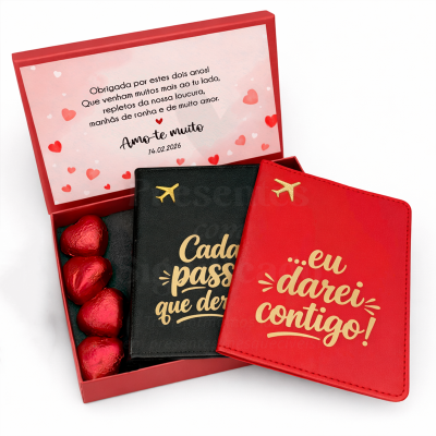 Caixa vermelha com chocolates em coração e dois porta-passaportes com textos em dourado, ícone de avião e mensagem no interior da tampa.