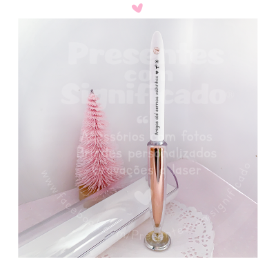 Caneta metálica dourada com ponta branca decorada, base redonda, pinheiro cor-de-rosa e caixa branca em fundo claro
