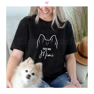 Mulher vestindo t-shirt preta com desenho de orelhas de cão e texto 'PROUD MOM Mimi', sentada com cão pequeno e chapéu castanho ao lado